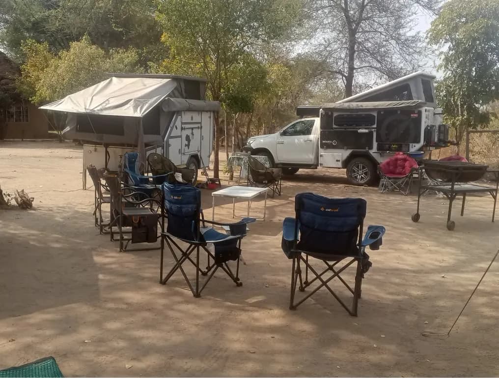 Pop-up camper and camp chairs on a sandy campsite pitch