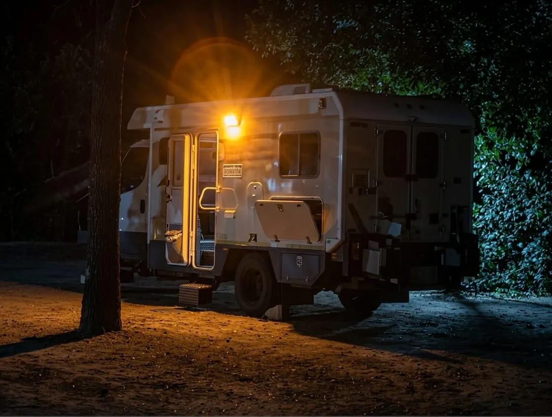 Expedition camper lit up at night under the trees