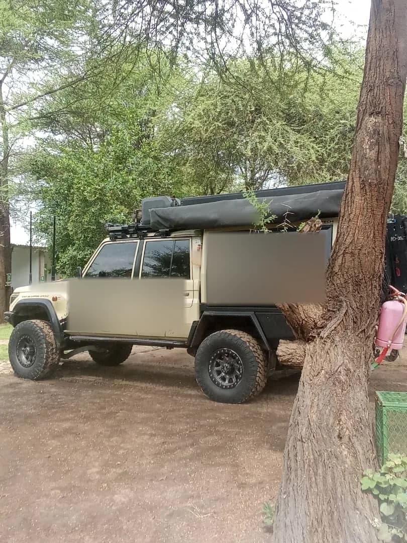 Expedition Land Cruiser with a roof awning parked under the trees on the campsite
