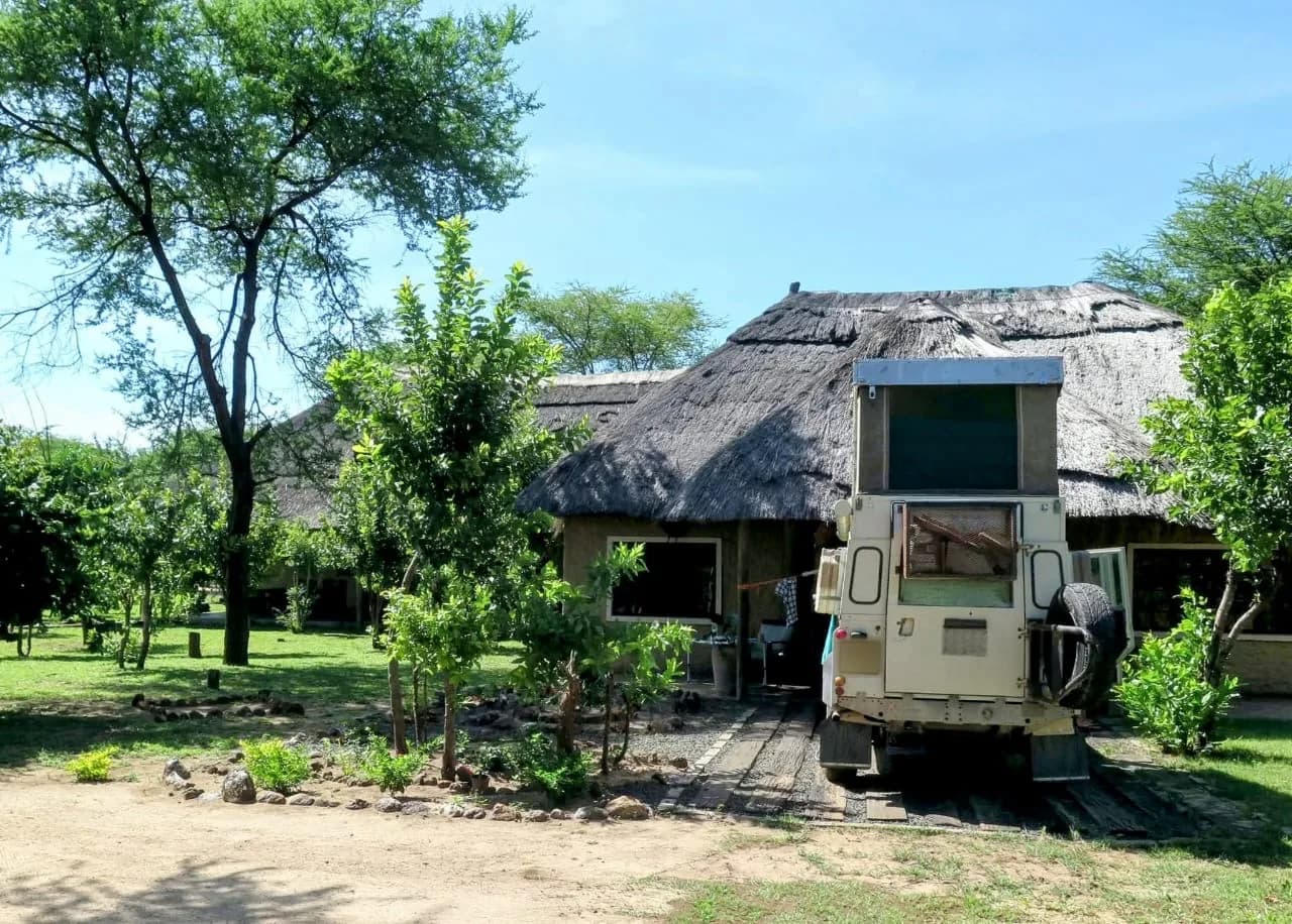 Thatched lodge building with an overland Land Rover and rooftop tent parked in front