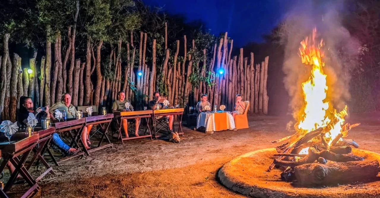 Guests seated at tables beside a roaring boma fire at night