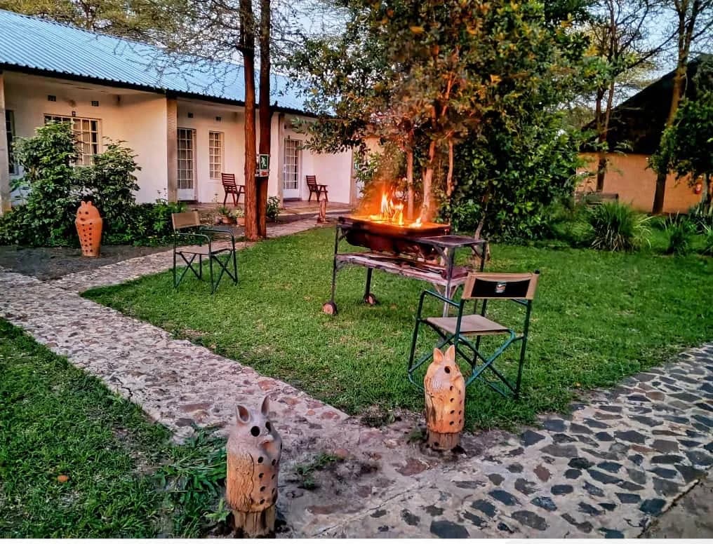 Lodge rooms and garden at dusk with a braai fire and clay owl lanterns