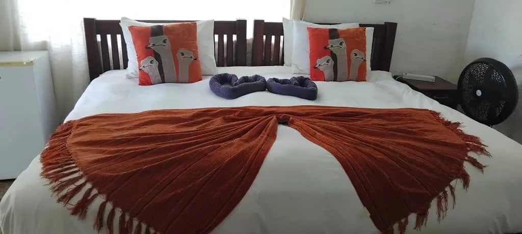 Double bed with ostrich-print cushions, towel hearts and an orange throw